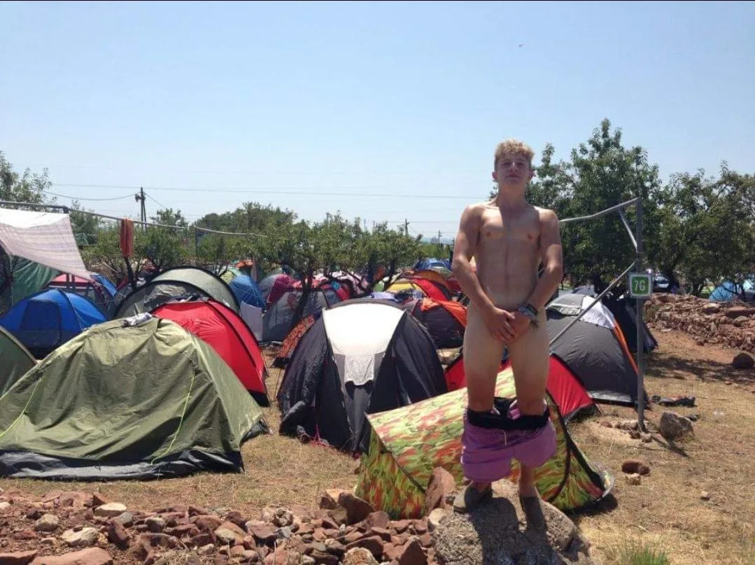Sunbaked festival lad standing nude with hands on cock amid tent chaos