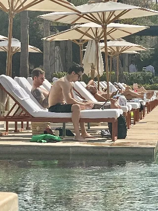 Tom Holland shirtless by poolside, lean muscles gleaming under sun, relaxed on lounge chair