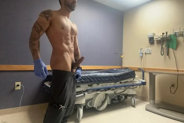 Muscular tattooed guy in medical gloves pulls pants down to expose hard cock and balls