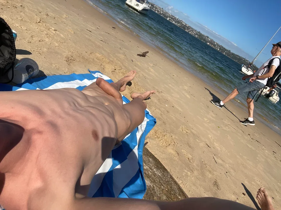 O rapaz da praia ensolarado se espalhou pela bunda em toalha, pau relaxado e visível em plena visão frontal