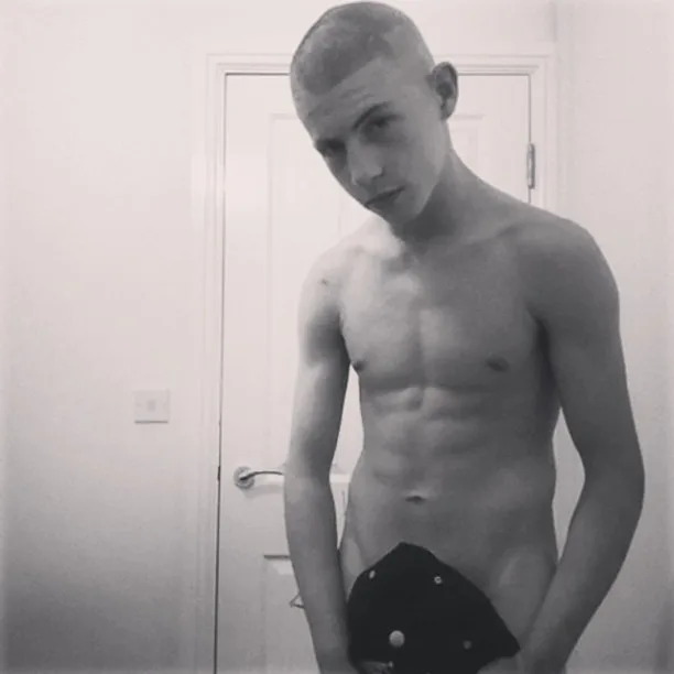 Shirtless scally lad with buzzcut and low-slung cap, bare torso gleaming in monochrome