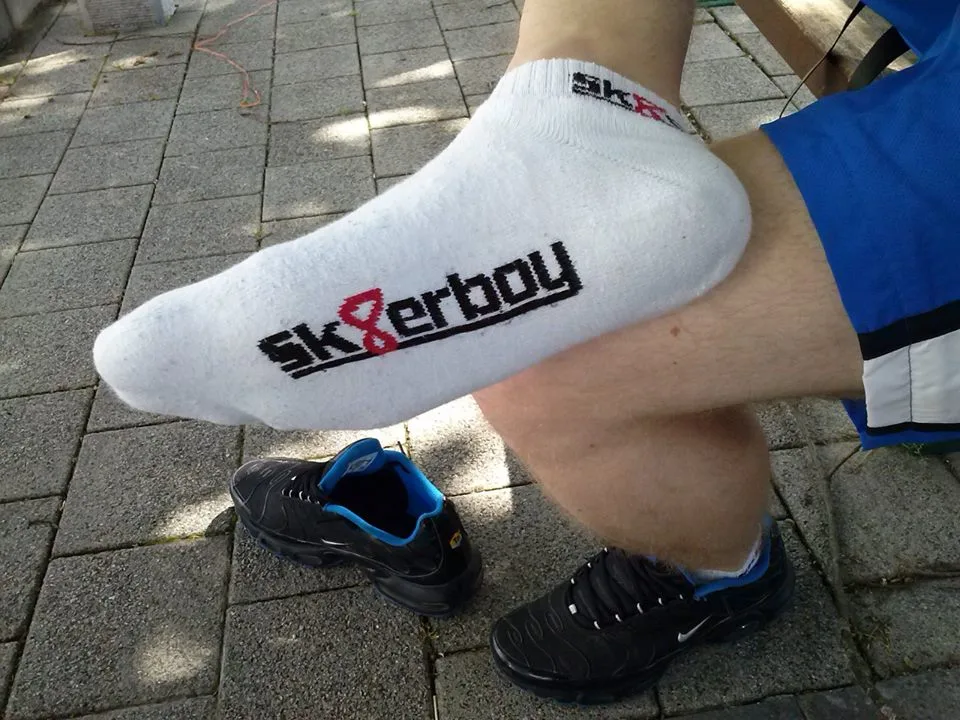 Pé de sk8erboy com meia flexionado sobre tênis, shorts azuis, provocação ao ar livre