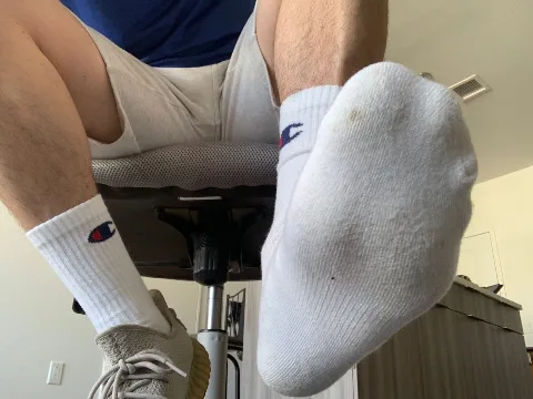 Guy in socks and shorts lounging with feet up, one shoe on, one bare socked foot flexed