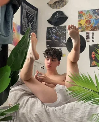Curly-haired lad in white briefs lifts bare feet high, soles on display for foot fetish fans