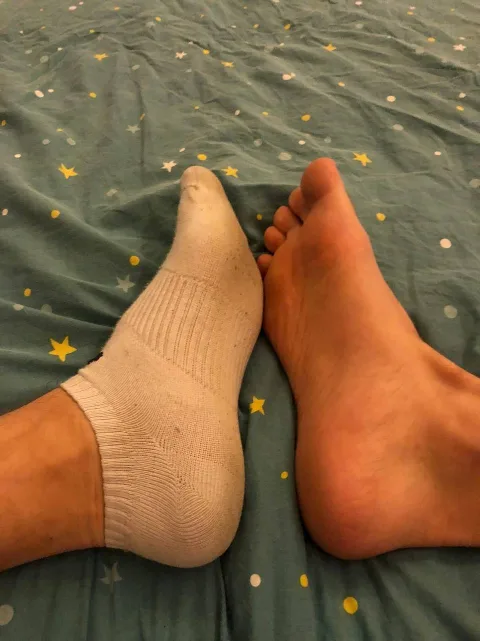 Sock-clad foot teasing bare sole on starry sheets, intimate foot-fetish moment