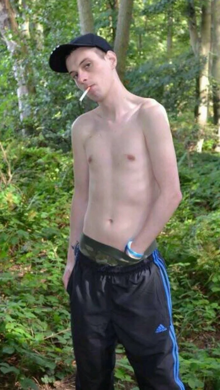 Shirtless scally lad in Adidas tracksuit pants and cap smokes while flashing camo boxers in the woods